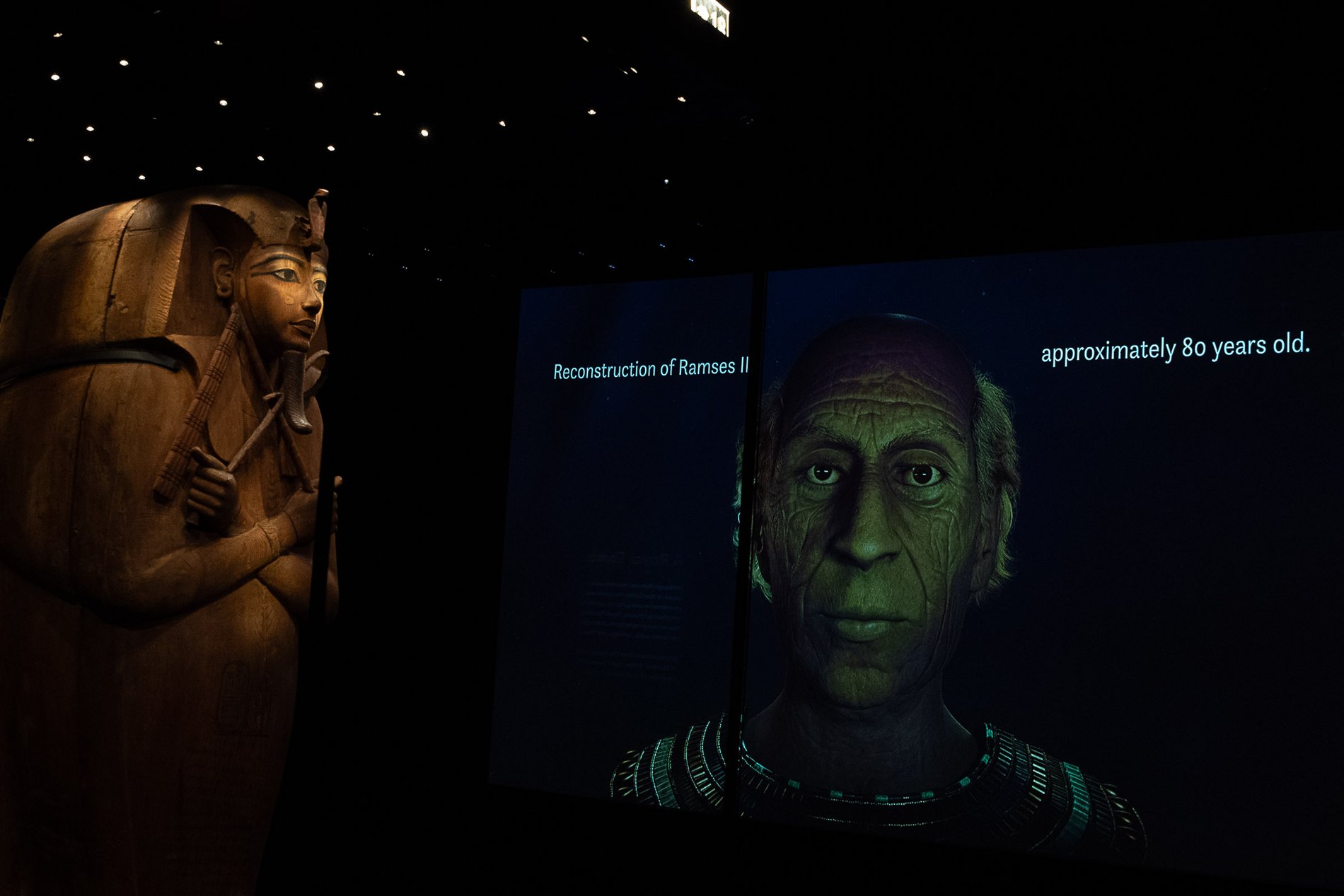Ramses' gilded coffin gazes toward a large screen showing a forensic reconstruction of the king in old age, at about eighty.